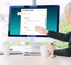 A woman pointing at a computer monitor displaying a "CUSTOMER REVIEWS" dashboard with a five-star rating.