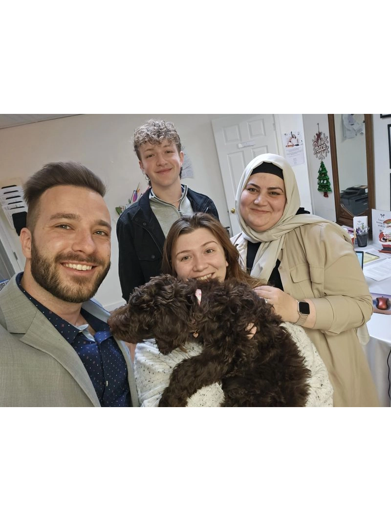 A group of four people poses together indoors, one holding a fluffy brown dog, surrounded by a cozy atmosphere and cheerful decor.